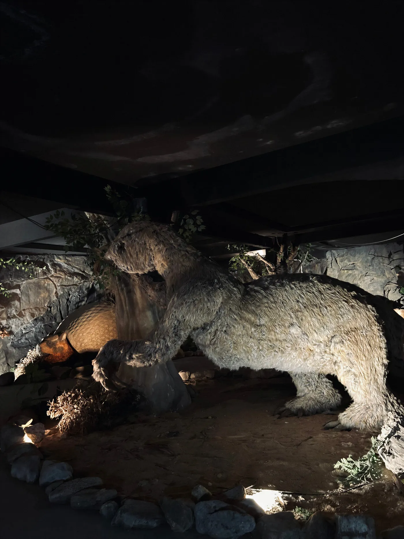 Reconstrução de uma preguiça-gigante apoiada em um tronco, com um gliptodonte ao fundo.
